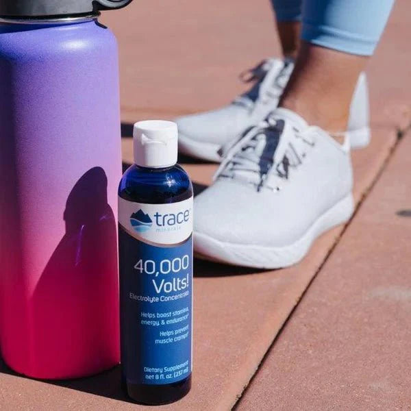 40,000 Volts - Electrolyte Concentrate - 237ml bottle by Trace Minerals next to purple-pink water bottle and person in sneakers