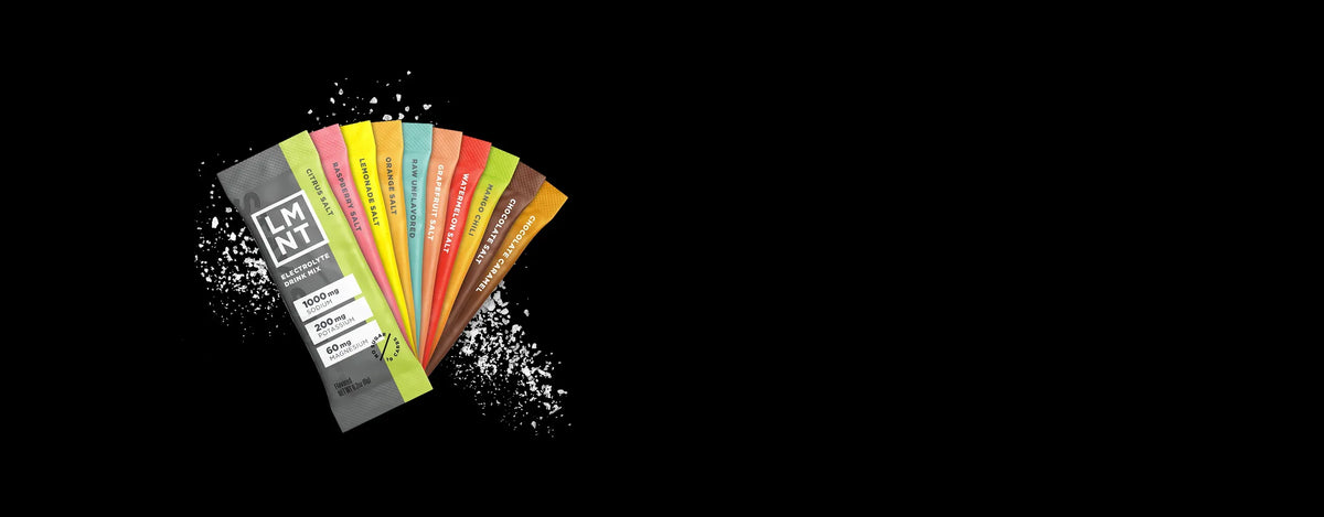 Array of LMNT electrolyte drink mix stick packs in multiple bright flavors, arranged in a fan shape against a dark background with scattered salt crystals.