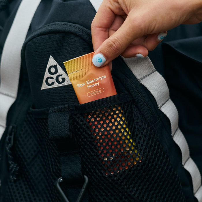Sodii Raw Electrolyte Honey sachet being placed in a backpack pocket