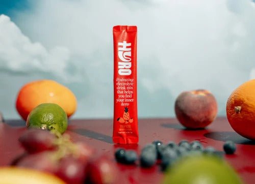 Hyro Single Stick packet standing on table surrounded by fresh fruits like blueberries, lime, peach, and oranges.