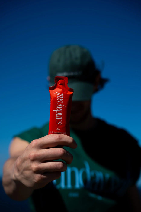 Person holding Sunday Salt Strawberry – Caffeine-Free Energy Gel - 50g against a clear blue sky background