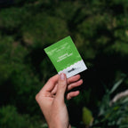 Hand holding Sodii's Salty Kiwi - 30 Sachets hydration salts pouch against a blurred natural green background