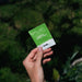 Hand holding Sodii's Salty Kiwi - 30 Sachets hydration salts pouch against a blurred natural green background