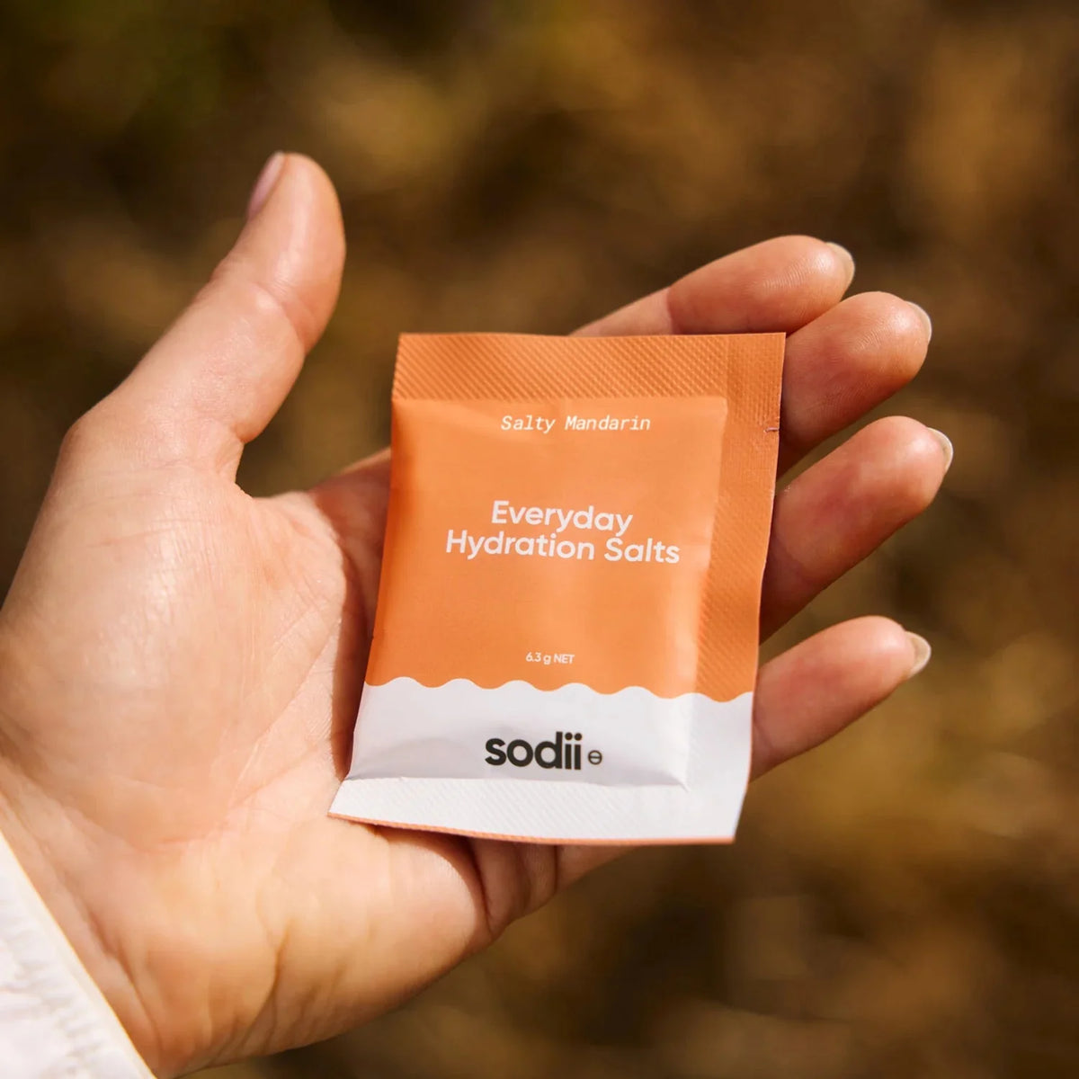 Hand holding a single orange and white sachet of Salty Mandarin - 30 Sachets by Sodii from the Electrolytes collection