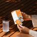 Person holding Salty Mandarin - 30 Sachets by Sodii with water bottle nearby on wooden surface in warm light