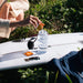 Person adding Sodii Salty Mandarin - 30 Sachets electrolyte sachet into water bottle on surfboard outdoors