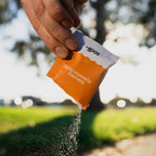Hand pouring salty mandarin electrolyte hydration salts from an orange and white Sodii sachet in outdoor natural light.