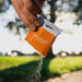 Hand pouring salty mandarin electrolyte hydration salts from an orange and white Sodii sachet in outdoor natural light.