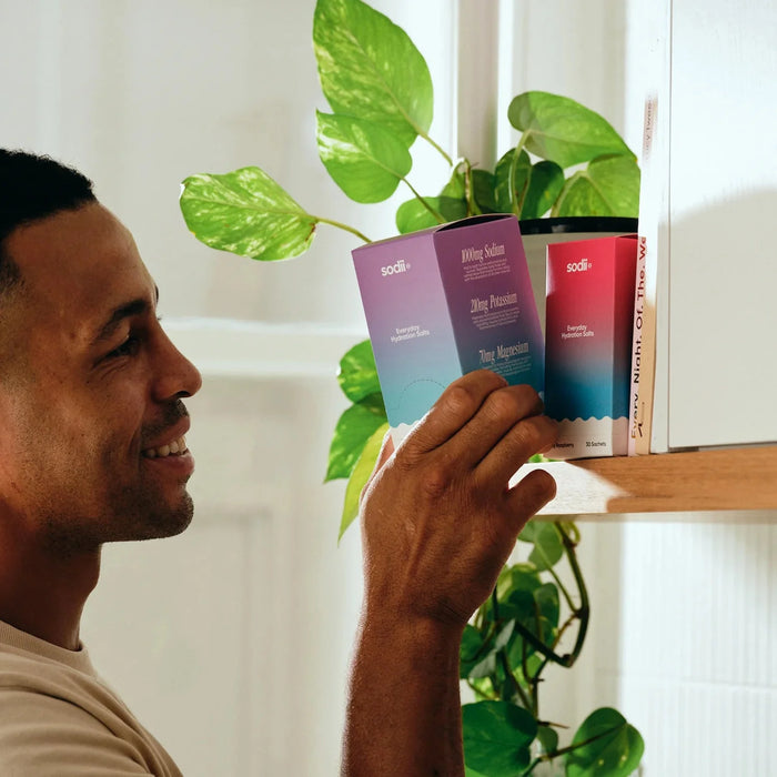 Man taking Salty Passionfruit - 30 Sachets by Sodii from kitchen shelf with green plant in background