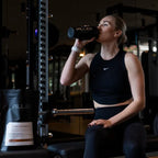 Woman in gym attire drinking from a shaker bottle with WPI - Vanilla - 1kg by PILLAR PERFORMANCE nearby